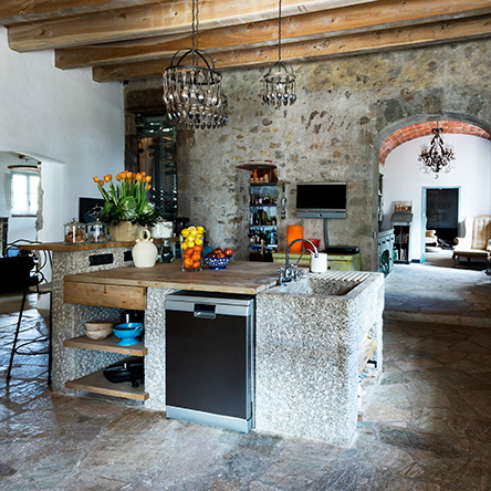 Kitchen in a Palamós Farmhouse designed by Ana Engelhorn with a stone centre island and exposed wooden ceiling beams