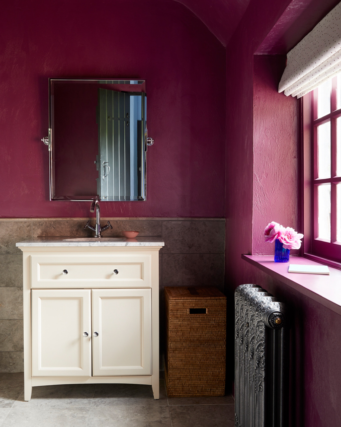 A dark red painted bathroom with a painted bathroom cabinet and bare metal radiator, all examples of bathroom interior design from Ana Engelhorn.