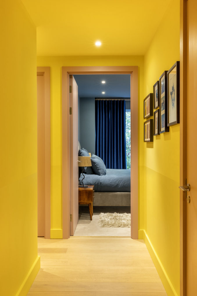 Corridor in an East London apartment designed by Ana Engelhorn interior design with bright yellow walls and ceiling leading to the master bedroom in blue colour tones
