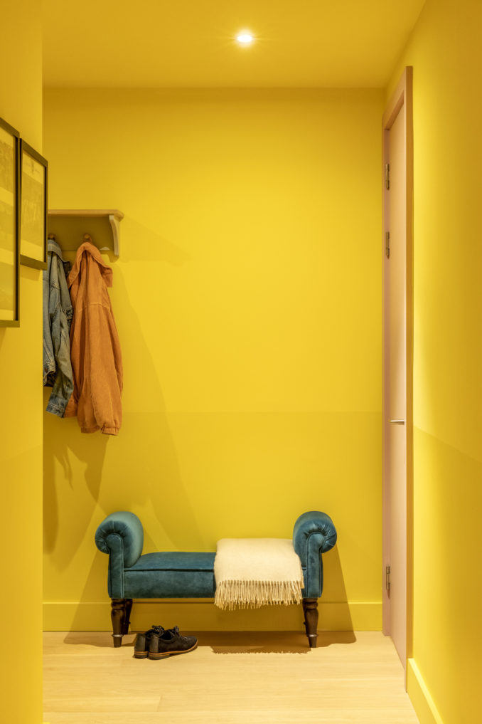 Padded stool against a bright yellow wall in an East London apartment designed by Ana Engelhorn interior design