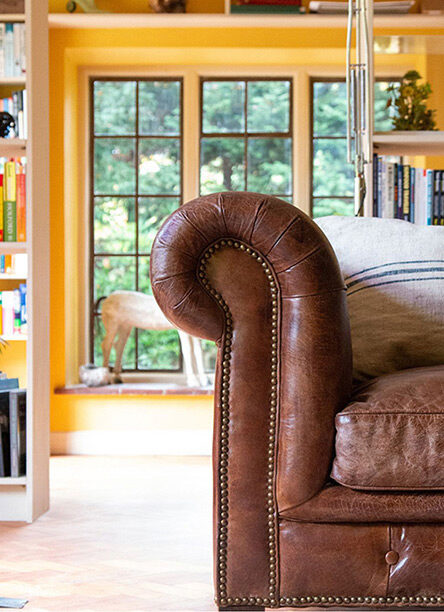 Detail of the arm of a leather sofa in a naturally bright room with yellow walls and book shelving can make the perfect breakaway space for a work from home meeting area