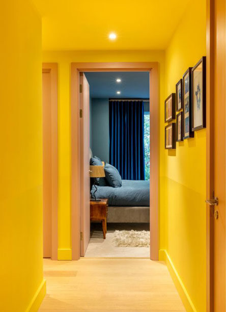 Corridor in an East London apartment designed by Ana Engelhorn interior design with bright yellow walls and ceiling leading to the master bedroom in blue colour tones.