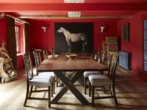 A stunning interior design makeover of a dining room in a Surrey farmhouse, with bold red walls and ceilings and natural wooden furnishings and chic accents.